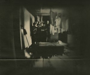 In Cellar of Their Bedeviled House, The Herrmanns - In a photograph by Nina Leen - gaze at a bookcase that mysteriously fell over From "House of Flying Objects" by Robert Wallace, in Life magazine, 1958 The Herrmanns and their two children, a girl and boy, stand next to the fallen bookcase in the cellar, looking down at it with disturbed expressions. Mr. Herrmann appears serious, Mrs. Herrman has her arms crossed, the daughter appears curious, and the son is holding his hands at his chest. Clothes hang on a line above beside the fallen bookcase.