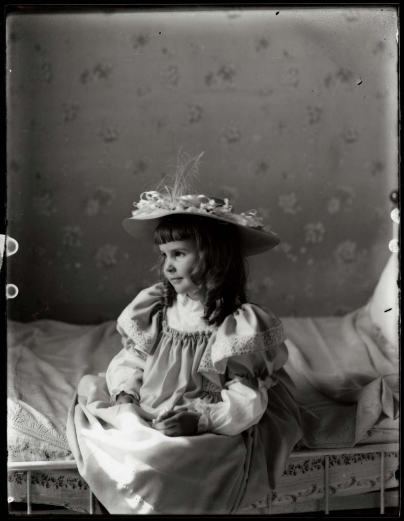 Young girl in a hat seated on a bed