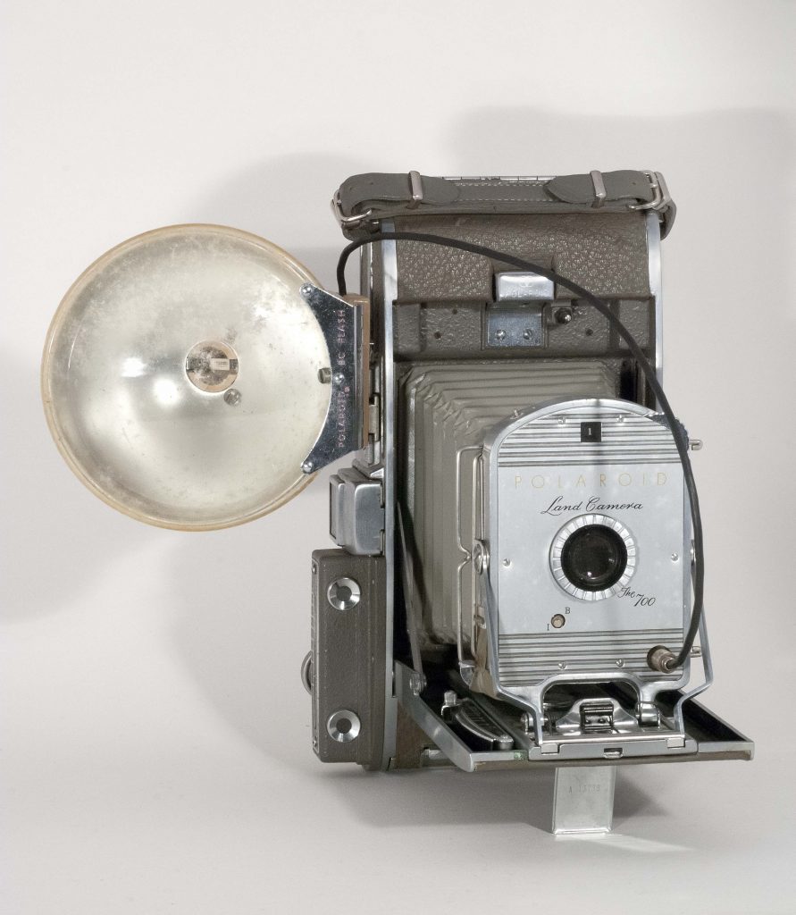 Polaroid 700, 1955-1957. Open, vertical, front view with flash attachment.