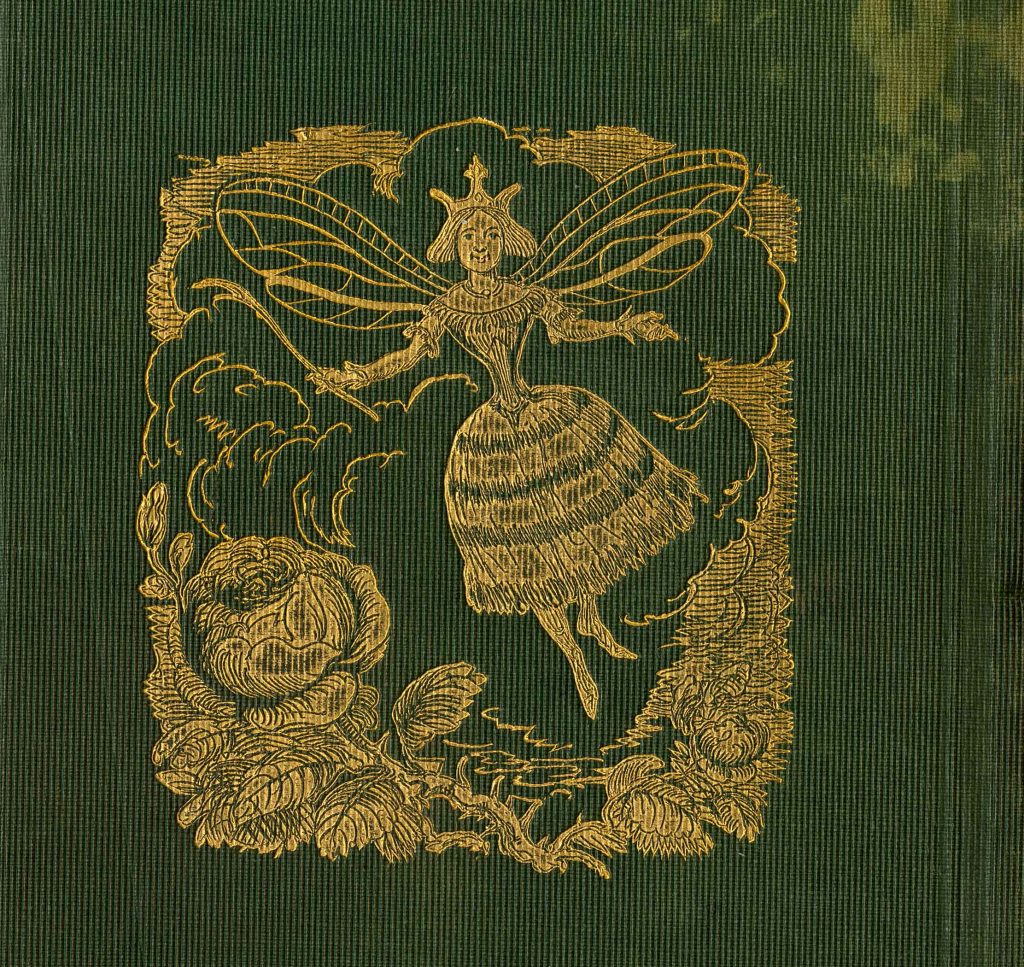 A gold fairy with wings is floating among a garden scene on a green cloth background. 