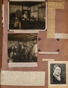 A page from a scrapbook with two newspaper clippings and three photographs. The first photograph shows a woman leaning back in a chair with a glasses-wearing man standing beside her. The second photograph shows a group of five people standing in front of a fireplace in a home. Some people are addressing the camera while others are not. The third photograph shows a white woman with short, slicked hair, a black top, and sparkling earrings facing to the right with her head and eyes facing the camera.