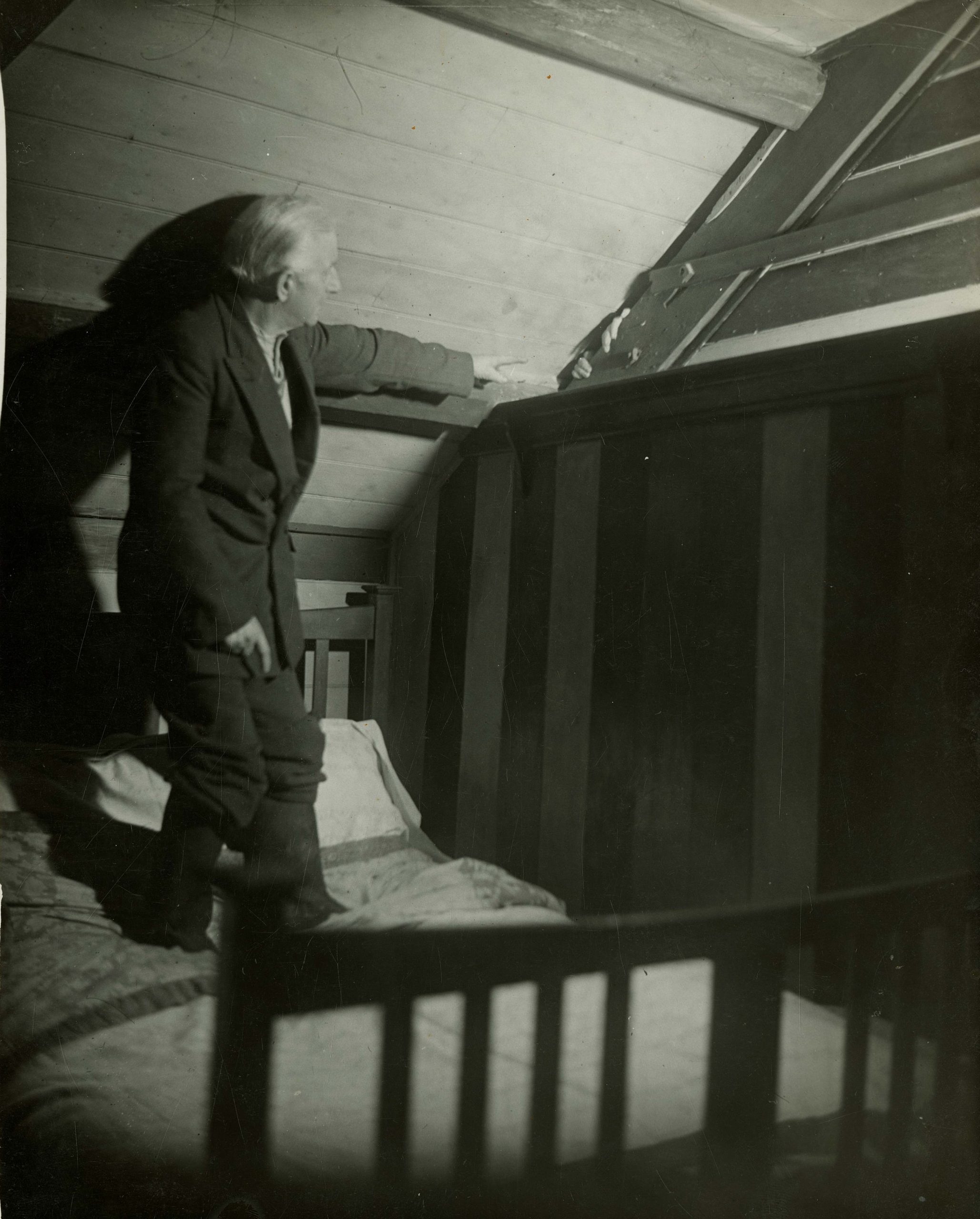 The image shows Mr. Irving standing on the bed in his room. He is pointing to the fingers of Mrs. Irving, coming through a slit in the slanted rafter connected to their daughter Voirrey's room; she is demonstrating how Gef has appeared.