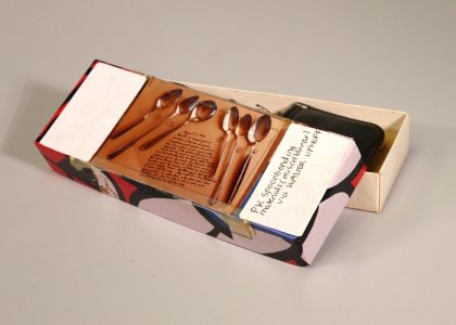 Open rectangular box with the printed photograph of 6 spoon on its lid. On the right side is a handwritten label.