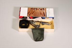 Open rectangular box with a lid with with a photograph of six spoons set to the side and miscellaneous items inside of the box itself.