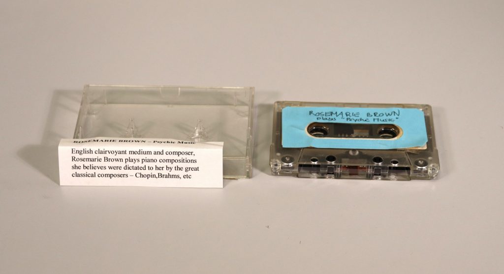 Cassette tape next to cassette casing with a folded piece of paper on top of it.