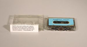 Blue cassette tape next to cassette casing with a folded piece of paper on top of it.