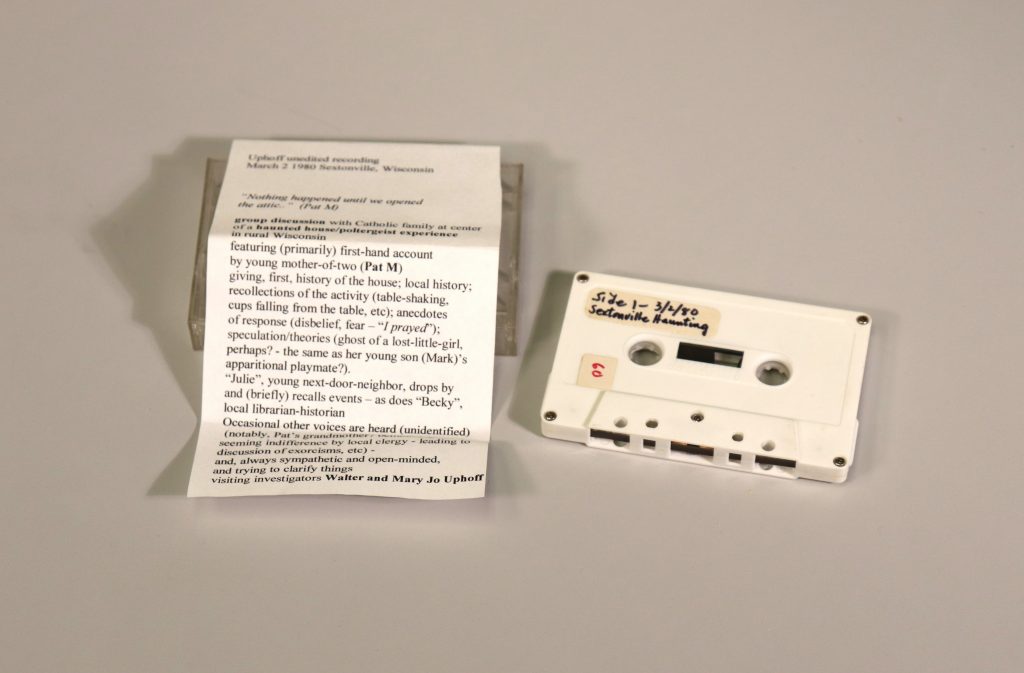 Cassette tape with handwritten label on its upper left corner, next to a printed piece of paper on top of a cassette case.