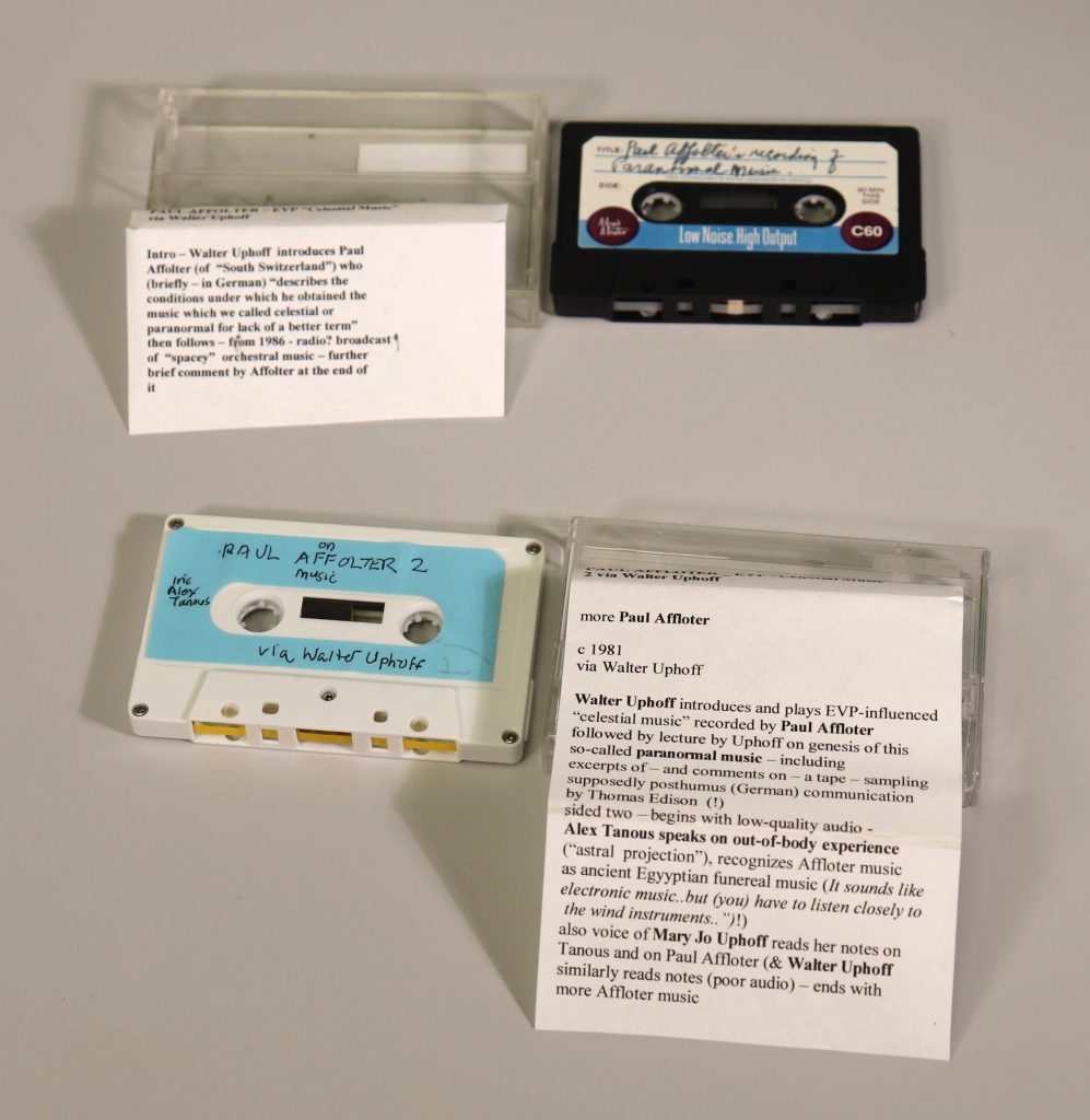 Two cassette tapes next to cassette cases and printed paper slips.