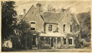 A Gothic-style house with two floors, three chimneys, and a front porch. The house is flanked by trees and slightly overgrown.