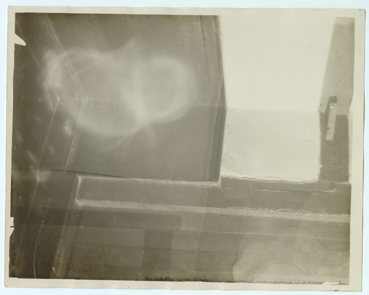 Photograph of an apparition at Ash Manor. Indistinguishable blobs of light appear in the top left and bottom right corner of the image.