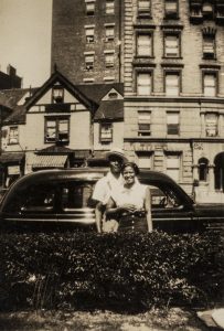 Couple standing in front of black car with apartment complex in background