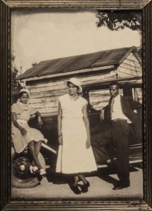 two women one man posing in front of black car