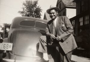 Man standing with his foot on the rear bumper of car.