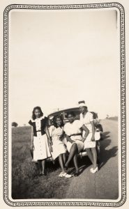 Four women sitting on and standing next to car.