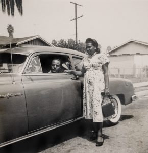 woman standing next to car with man sitting in driver's seat.