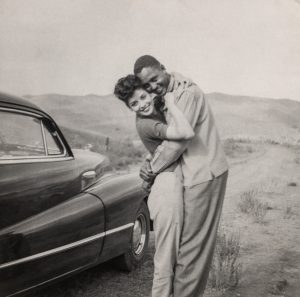 Man and woman hugging with car to the side.