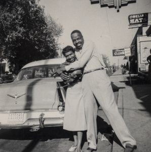 man hugging woman in front of car on city street.