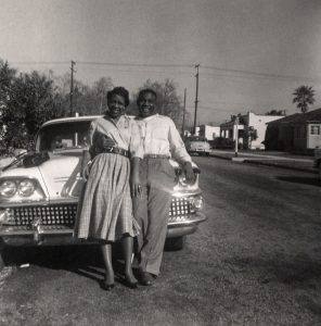 Couple standing and hugging in front of car on neighborhood street.