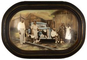 Colored, oval framed image of a family in front of their blue sedal