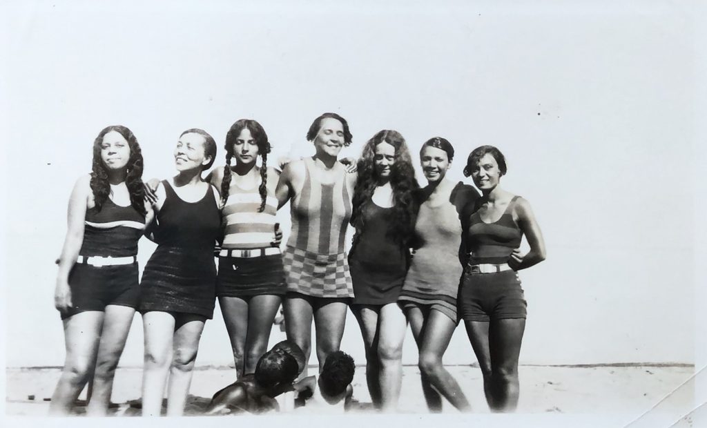 Group of seven women standing on the beach shore.