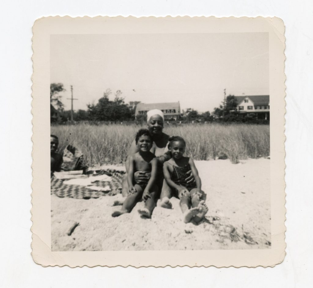 A woman and two kids sitting on the beach.