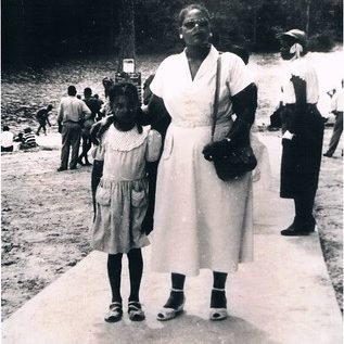 A woman and child stand on the sandy beach shore of Prince Edward Lake.