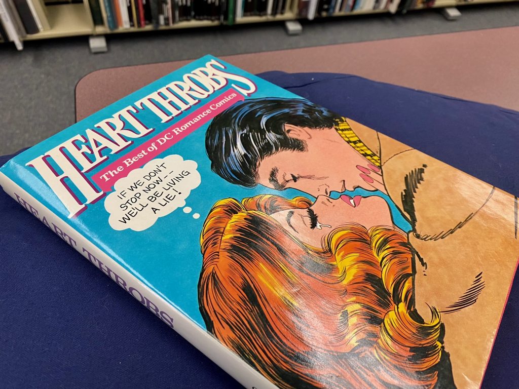 Front cover of "Heart Throbs: The Best of DC Romance Comics" in the Special Collections reading room. The cover features a woman and man embracing on the verge of a kiss. The woman is shedding tears and the thought bubble above her head reads: "If we don't stop now — we'll be living a lie!"