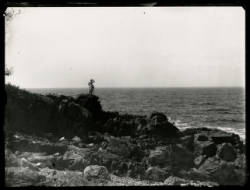 Black and white photograph of a person standing on a rocky shoreline