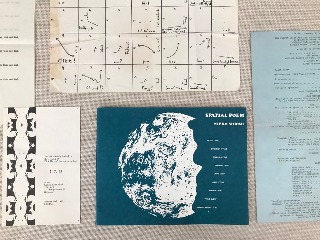 Materials from the Dick Higgins Collection displayed in Case 5. The items are laid flat in the case, including "Spatial Poem" by Mieko Shiomi, hand-written musical notations by Dick Higgins, and an invitation for Dick Higgins’ first solo exhibition at Galerie René Block, Berlin amongst others.