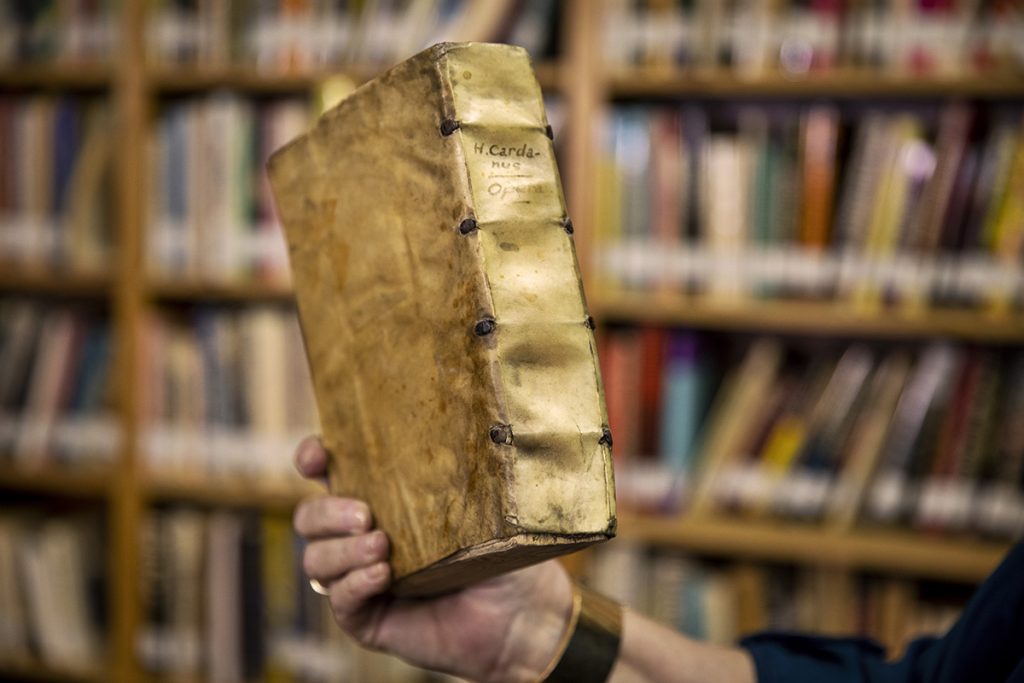 Hand holding a rare book in front of a row of bookshelves.